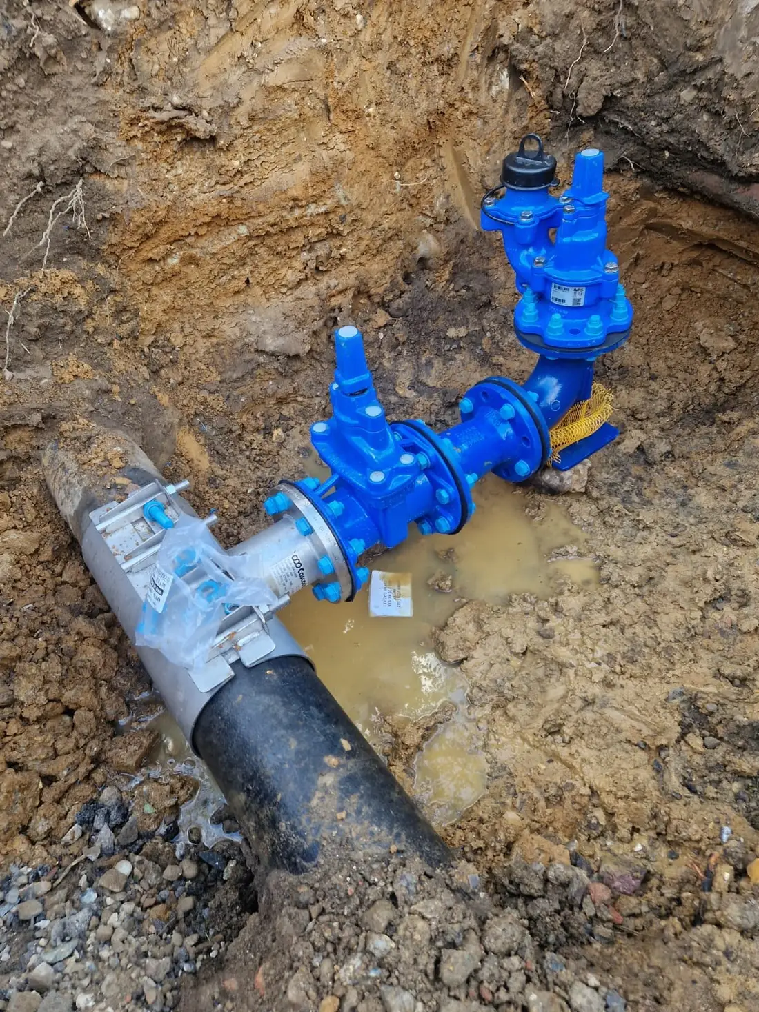 Blue valve and hydrant assembly connected to a water main by a tapping tee in an excavation