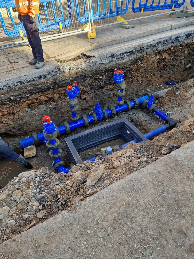 Blue water main pipework with valves and a chamber in a roadside excavation