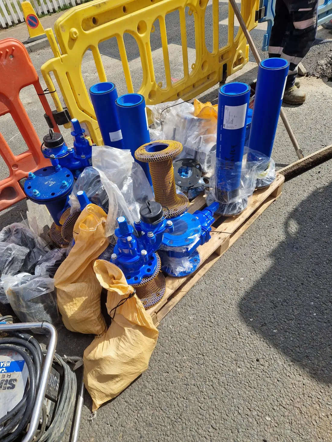 Blue water main valves, pipe sections and fittings stacked on a pallet on site